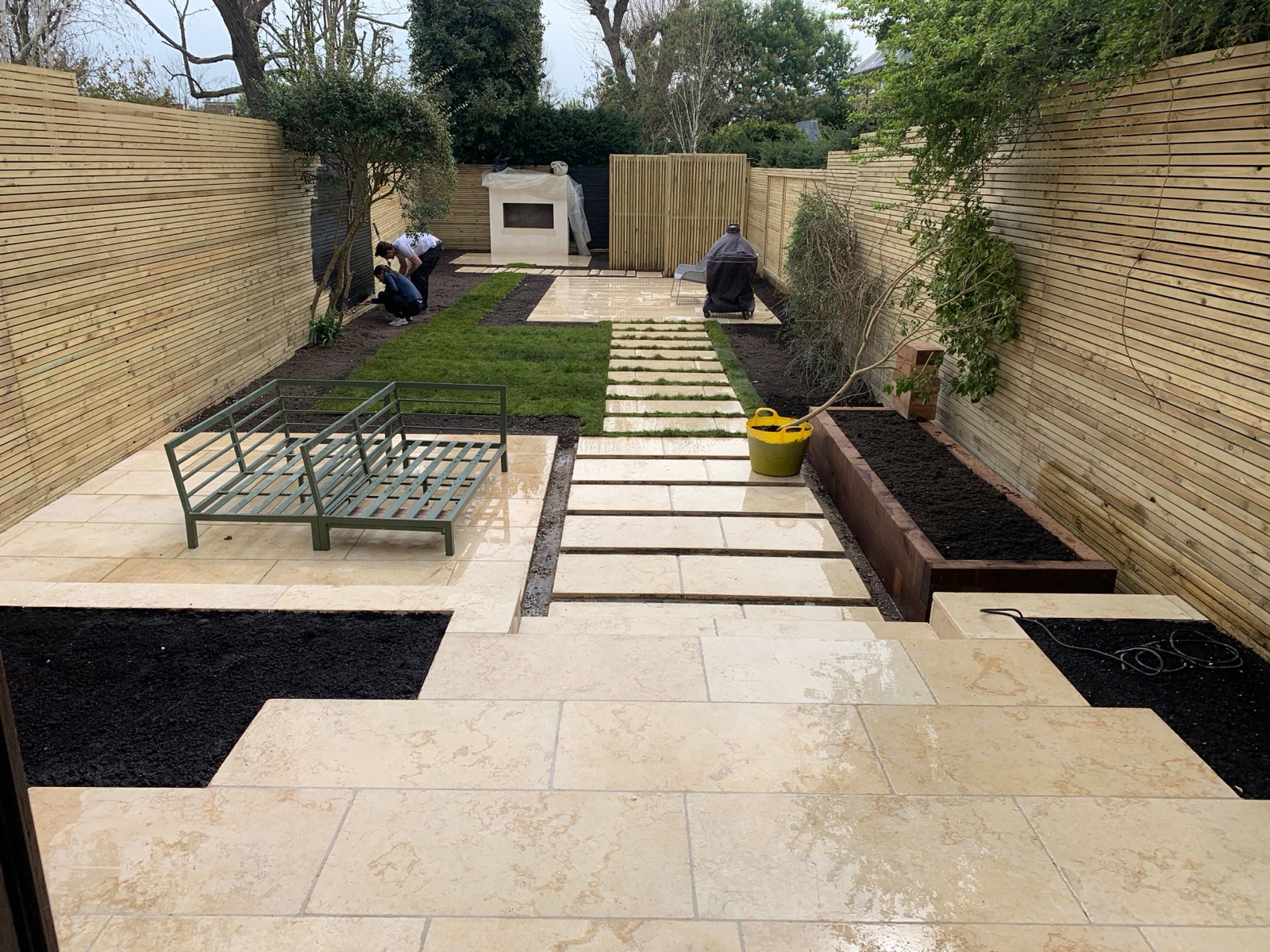 Team laying travertine paving slabs in a full garden redesign
